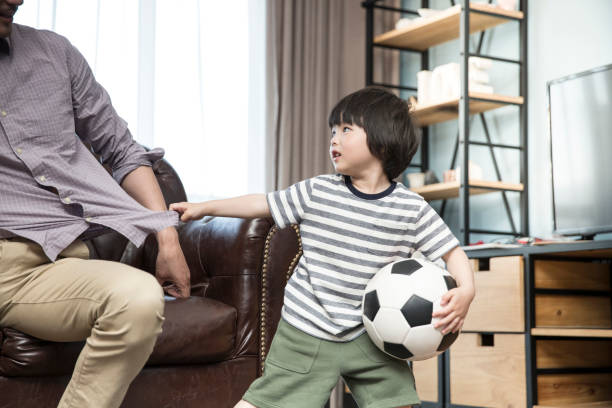 petit garçon tirant sur le manteau de son père dans le salon familial, qui veut que papa sorte et joue au football avec lui - photo d’archives - men suit holding human finger photos et images de collection