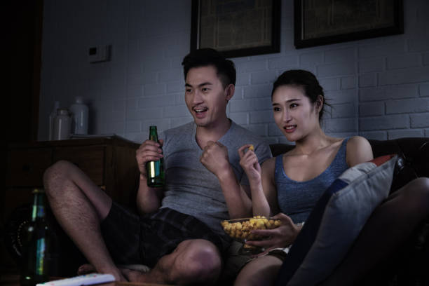 Couple excitedly watching live sports on TV on the living room couch late at night - stock photo stock photo