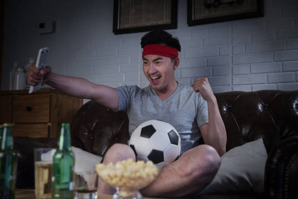 Man watching a soccer game on TV on the living room couch late at night, drinking beer ,excited expressions - stock photo stock photo