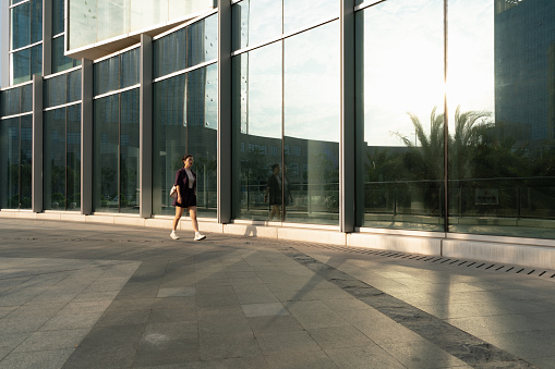 Lady walking by the glass curtain wall in sunlight