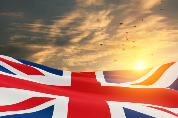 Photo of National flags of United Kingdom with flying birds on sunset sky background.