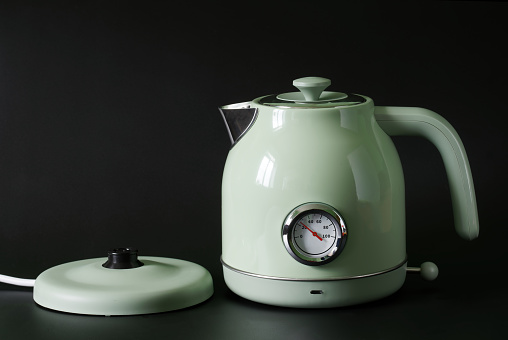 Fashionable green metal electric kettle and rotating stand on a black background. Close-up