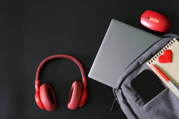 istock Gray backpack or laptop bag with mobile phone, notepad, pen and laptop on black background next to red headphones and mouse. Study, travel and lifestyle with gadgets. Copy space. 1436036440