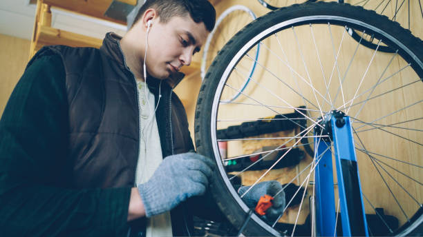 istock Concentrated mechanic is fixing spokes on bicycle wheel with special tools while servicing bike and listening to music through earphones. Maintenance and profession concept. 1436037539