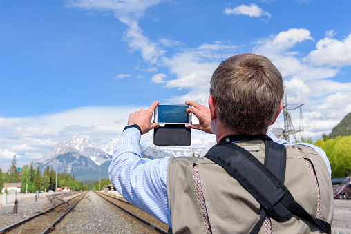 A tourist man taking pictures of Train Station in Banff by using mobile phone, Alberta, Canada