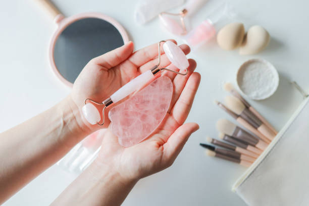istock Woman holding gua sha tool and cosmetic over white table, top view 1436039440