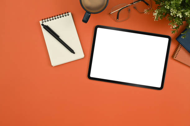 istock Flat lay digital tablet with white empty screen, notepad, glasses and coffee cup on orange background. 1436042115