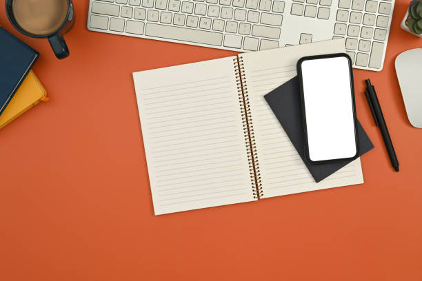 istock Top view smart phone with blank screen, notepad, coffee cup and keyboard on orange background. 1436042126