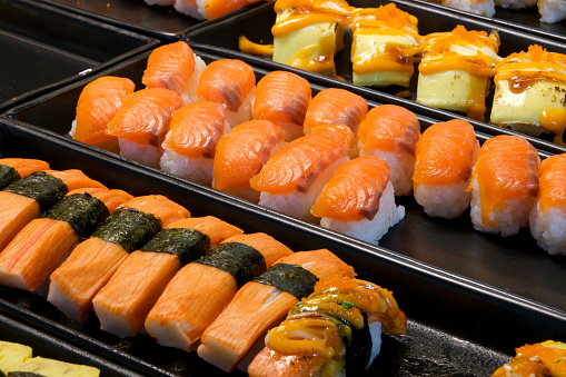 Selective focus photo of nigiri and sushi dishes which are famous in traditional Japanese cuisine that are detailed of ingredients with salmon, crab sausage 
 and cheese and sauces top on it