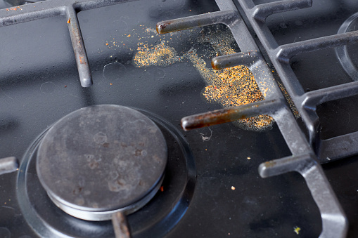Dirty unclean kitchen black stove with dried food spots, fat stains and soup boil over leftovers. Black stainless cooktop with gas burner stained in remains of fat food, fry spots and oil splatters