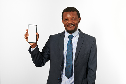 Smiling african american black man in business suit with smartphone blank mockup in hand, white wall background. Portrait of happy black businessman holding white phone mock up for advertising