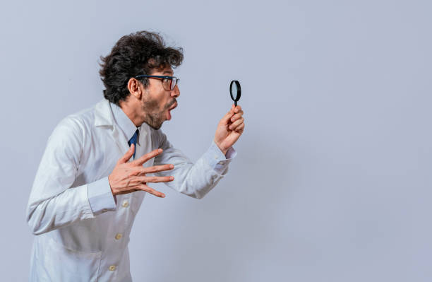 istock Scientist holding a magnifying glass looking to the side, Man in a white coat with a magnifying glass looking advertisement, Surprised scientist observing with a magnifying glass to the side 1436043936