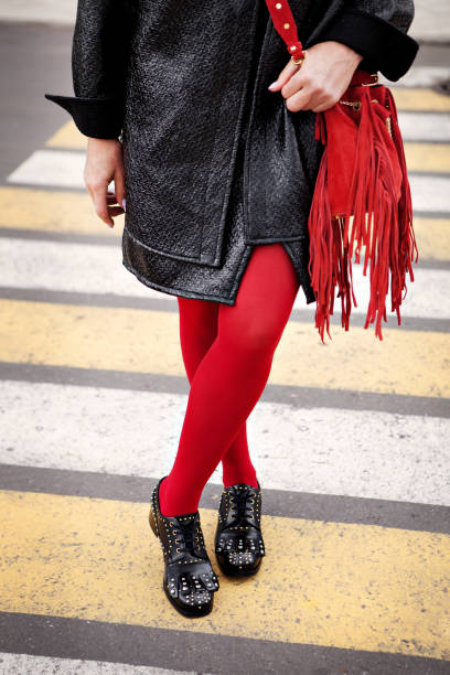Woman in red color tights, black shoes with rivets and hand bag with fringe standing on pedestrian crossing. Fashion details for stylish extravagant women Woman in red color tights, black shoes with rivets and hand bag with fringe standing on pedestrian crossing. Fashion details for stylish extravagant women older women short skirts stock pictures, royalty-free photos & images