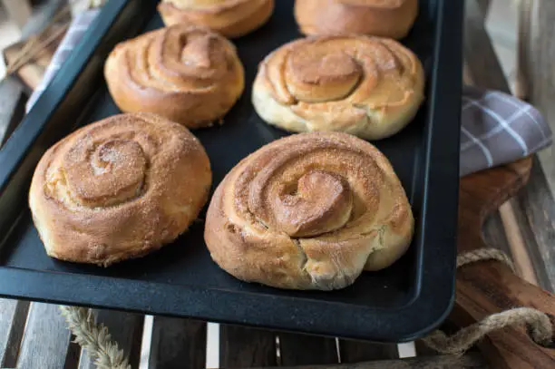 Fresh and homemade baked cinnamon rolls. Served lined up and hot on a baking sheet isolated on wooden and blurred background