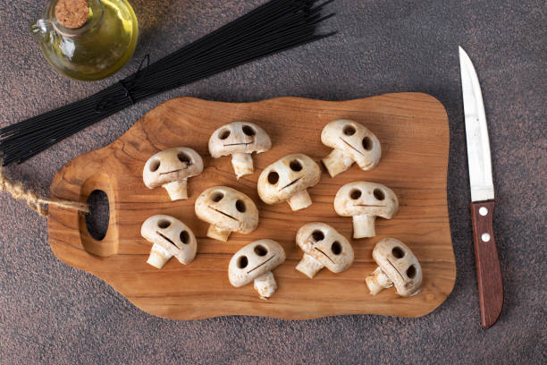 Mushrooms in the form of skulls on wooden board, also olive oil and raw black spaghetti, Edible Halloween cooking concept stock photo
