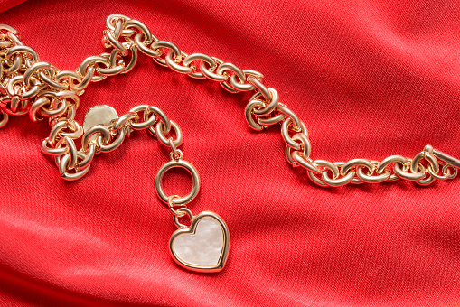 Gold chain with nacre heart pendant on red fabric background