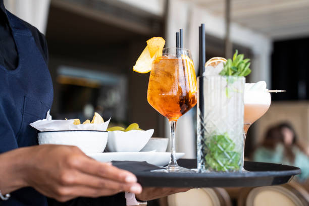 Closeup of tray with cocktails and appetizers - Spritz and mojito served by an African waitress in the restaurant bar Closeup of tray with cocktails and appetizers - Spritz and mojito served by an African waitress in the restaurant bar food and drink establishment stock pictures, royalty-free photos & images