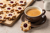 Star shaped linzer cookies with raspberry jam , homemade, and big cup of coffee with milk.