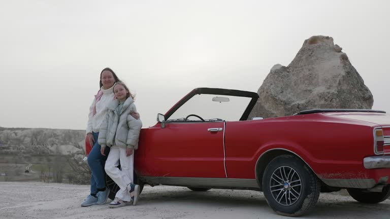 Zooming out shot of mother and daughter standing by red car on mountain