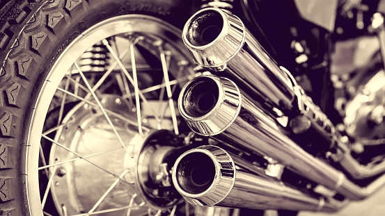 Beautiful exhaust system with three chrome pipes on the side of the historic motorcycle - a sepia toned image