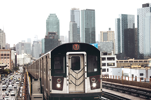 Modern cityscape of Midtown Manhattan on the background while a train of the NYC Subway passing by in the Queens