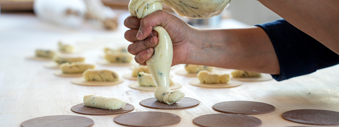 Horizontal banner or header with woman prepare fresh made ravioli inside pasta factory. Using a pastry bag or sac a poche to make stuffed pasta ravioli, culurgiones, agnolotti. Focus on stuffed