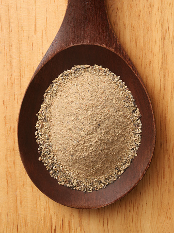 Top view of wooden spoon with ground cardamom seeds on it