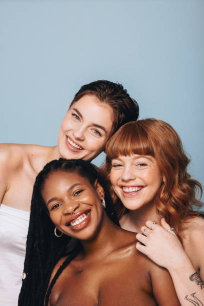 Happy women with different skin tones smiling at the camera in a studio Happy women with different skin tones smiling at the camera in a studio. Group of body confident young women embracing their natural beauty. Three body positive young women standing together. imperfection stock pictures, royalty-free photos & images