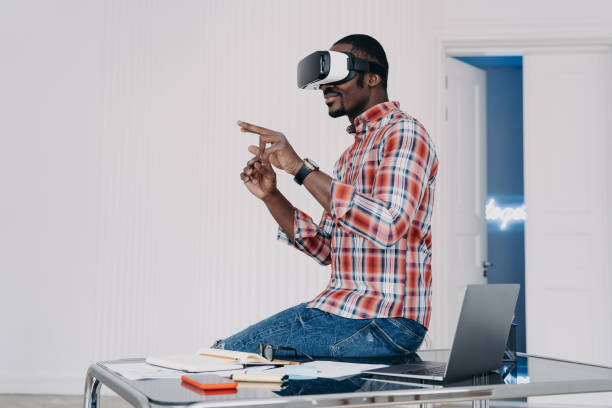 istock African american man in VR glasses interacts with virtual reality working in office, sitting on desk 1436061908