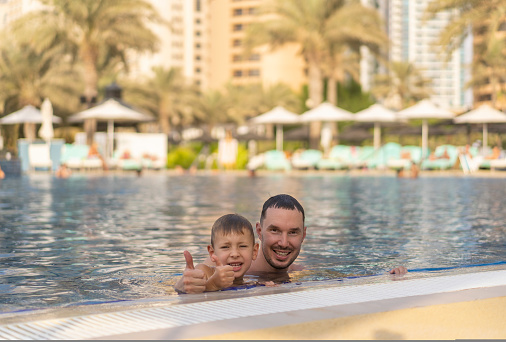 Father and son have fun in the pool in Dubai and show thumbs up. International Father's Day concept.