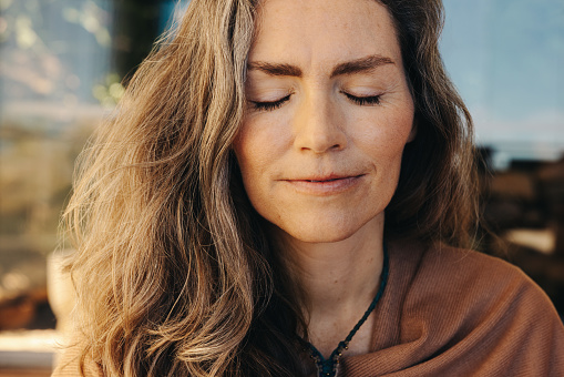 Meditation and self-healing. Senior woman meditating with her eyes closed and with a crystal necklace around her neck. Mature woman practicing a holistic lifestyle at home.