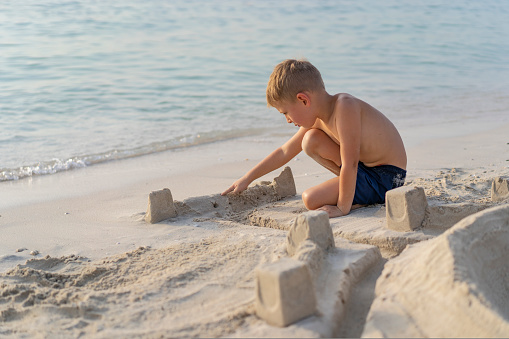 Little boy plays on the beach in Dubai and builds a sand castle.