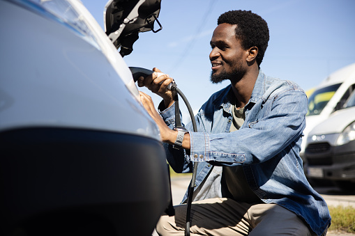 Portrait of a young African American man charging his electric van at the charging station