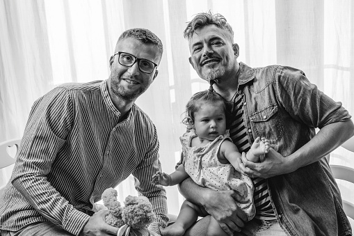 Portrait of happy LGBTQ family at home - Gay couple and their daughter - Diversity concept and LGBTQ family relationship - Black and white