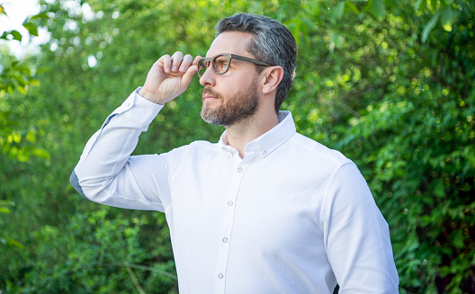 Professional man looking into distance in eyeglasses natural background, eyesight.