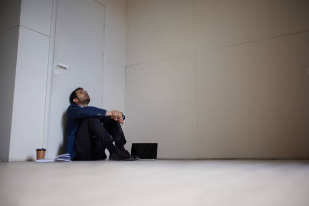 Portrait of young businessman sitting on floor in empty room. Business closure. Depression and crisis. Losing job and finances Portrait of young businessman sitting on floor in empty room. Business closure. Depression and crisis. Losing job and finances. Concept of business, challenges, work, occupation closing down sale stock pictures, royalty-free photos & images