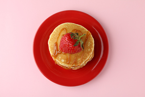 Plate with pancakes with strawberry and caramel on pink background