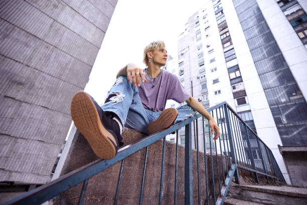 A teenage boy is sitting and posing in urban exterior surrounded by the buildings. stock photo