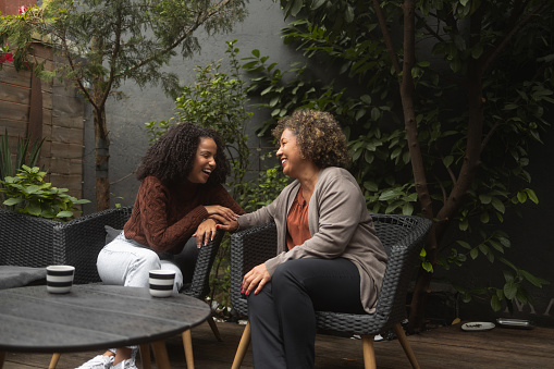 Shot of a young African-American woman bonding with her mother. They sit on the patio and have a coffee.