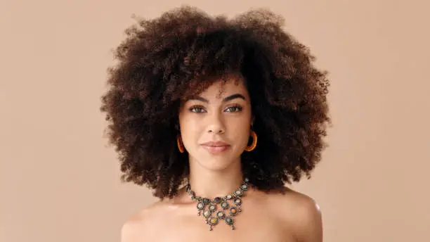 Photo of Black woman afro, portrait and confident face in beauty and style against a studio background. Beautiful isolated African American female proud model with necklace, jewelry and hairstyle for fashion