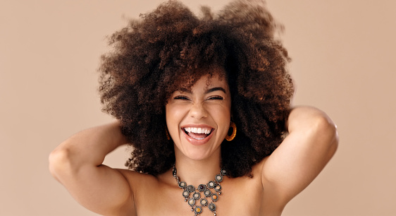 Romantic expression and light smile on the face of brown haired young woman. Natural, dense afro hair on the head of young beautiful model. Girl with vibrant, melanin-rich skin tone. Sincere look at the viewer.