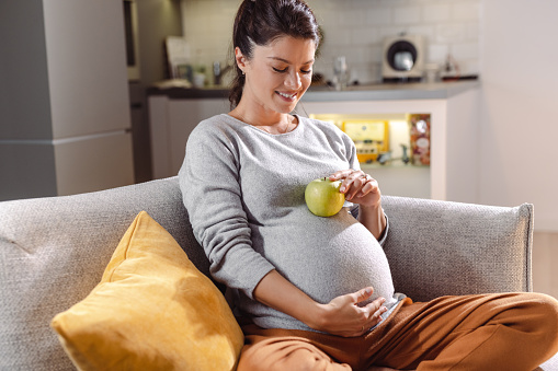 Beautiful pregnant woman holding a green apple as a symbol of healthy eating. Happy maternity and pregnancy concept
