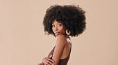 Young, black woman and with afro being relax, happy and confident with brown studio background. Portrait, mockup space and girl or lady pose for a fashion magazine cover, makeup brand and skincare.