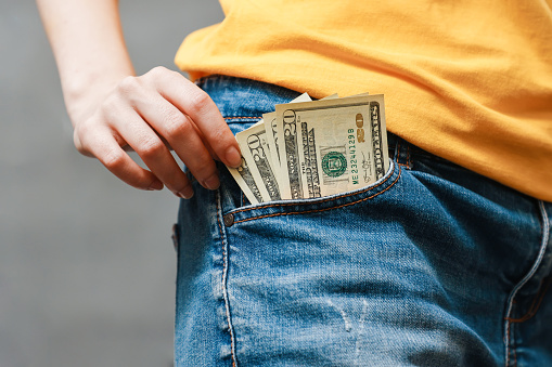 A woman's hand pulls American dollars out of her jeans pocket. Close-up. The concept of salary, savings and wealth
