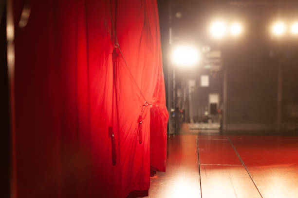 Actor is pulling red curtains in theatre with hand.
