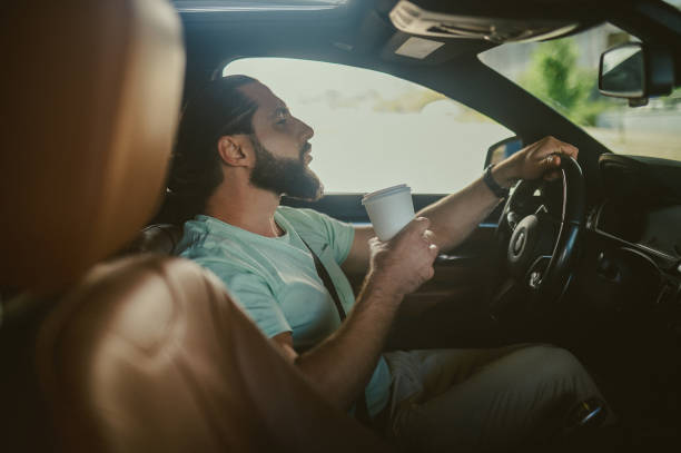 istock Young handsome dark-haired man holding a phone and driving a car 1436081227