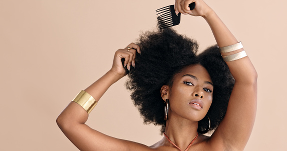 Black woman, hair and afro in portrait comb natural curls with confidence against earthy background. Model, girl and face hair care for beauty, wellness and fashion against cosmetic studio backdrop