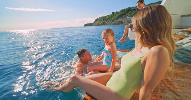 Happy family sitting on deck while enjoying in sea during sunny day.