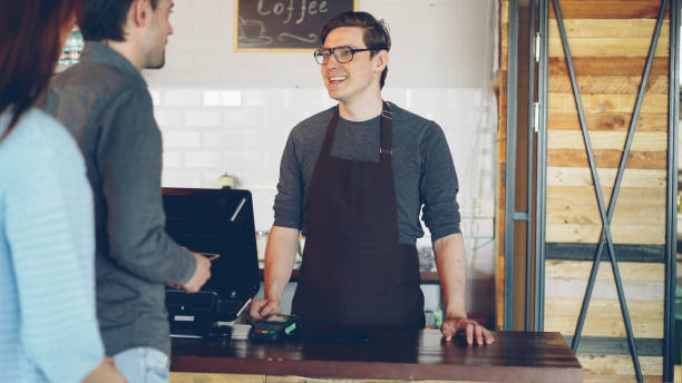 istock Cheerful friendly cashier is taking orders from customers standing in line, accepting payment and selling takeaway coffee 1436081911