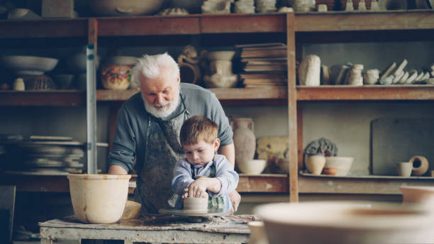 istock Caring grandfather experienced potter is teaching little boy how to work with clay on potter's wheel. Grandson is making mistake, patient grandpa is helping him. 1436086035